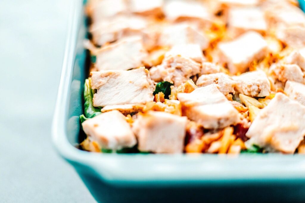 Close-up of a chicken dressing casserole being layered in a baking dish, showing shredded chicken, creamy sauce, and cornbread mixture evenly spread.