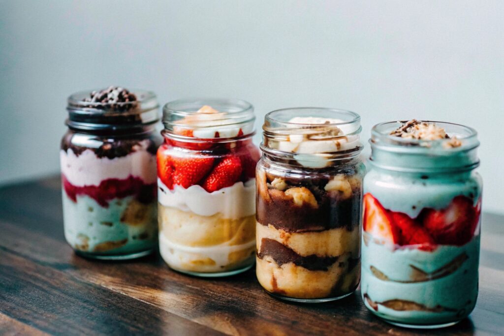 An assortment of banana pudding variations in mason jars, showing layers of strawberries, chocolate, and traditional ingredients