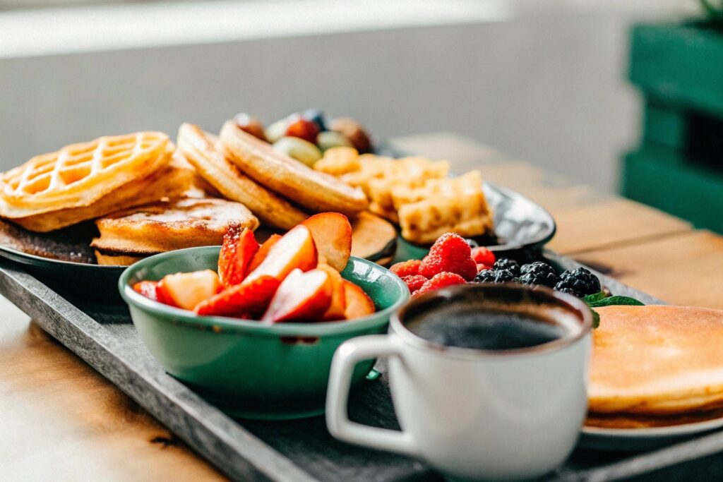 A colorful spread of pancakes, waffles, and fruits on a rustic wooden table with a cup of steaming coffee.