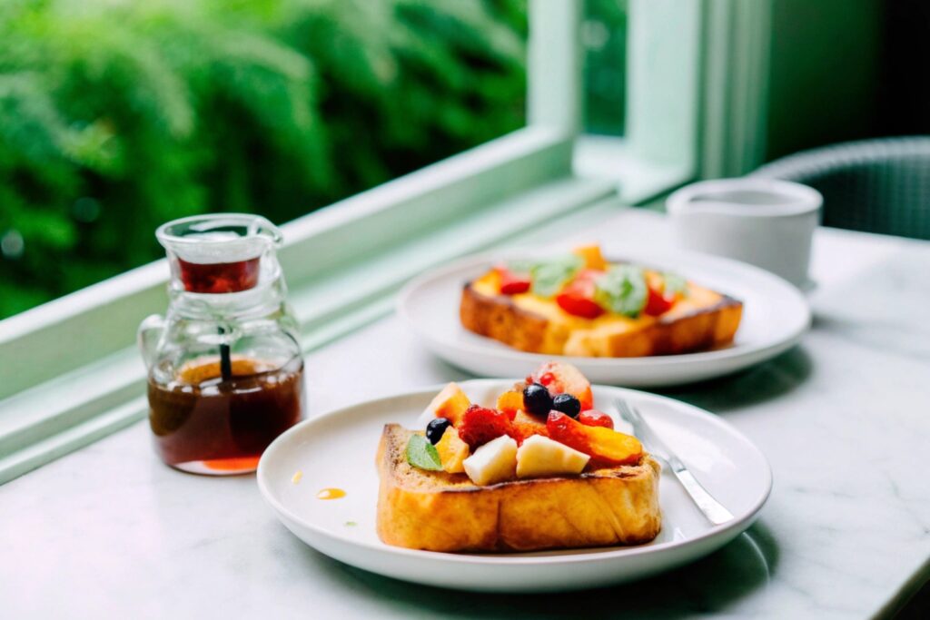 A cozy breakfast table setting with Hawaiian Roll French Toast served with fresh fruit toppings, syrup, and whipped cream