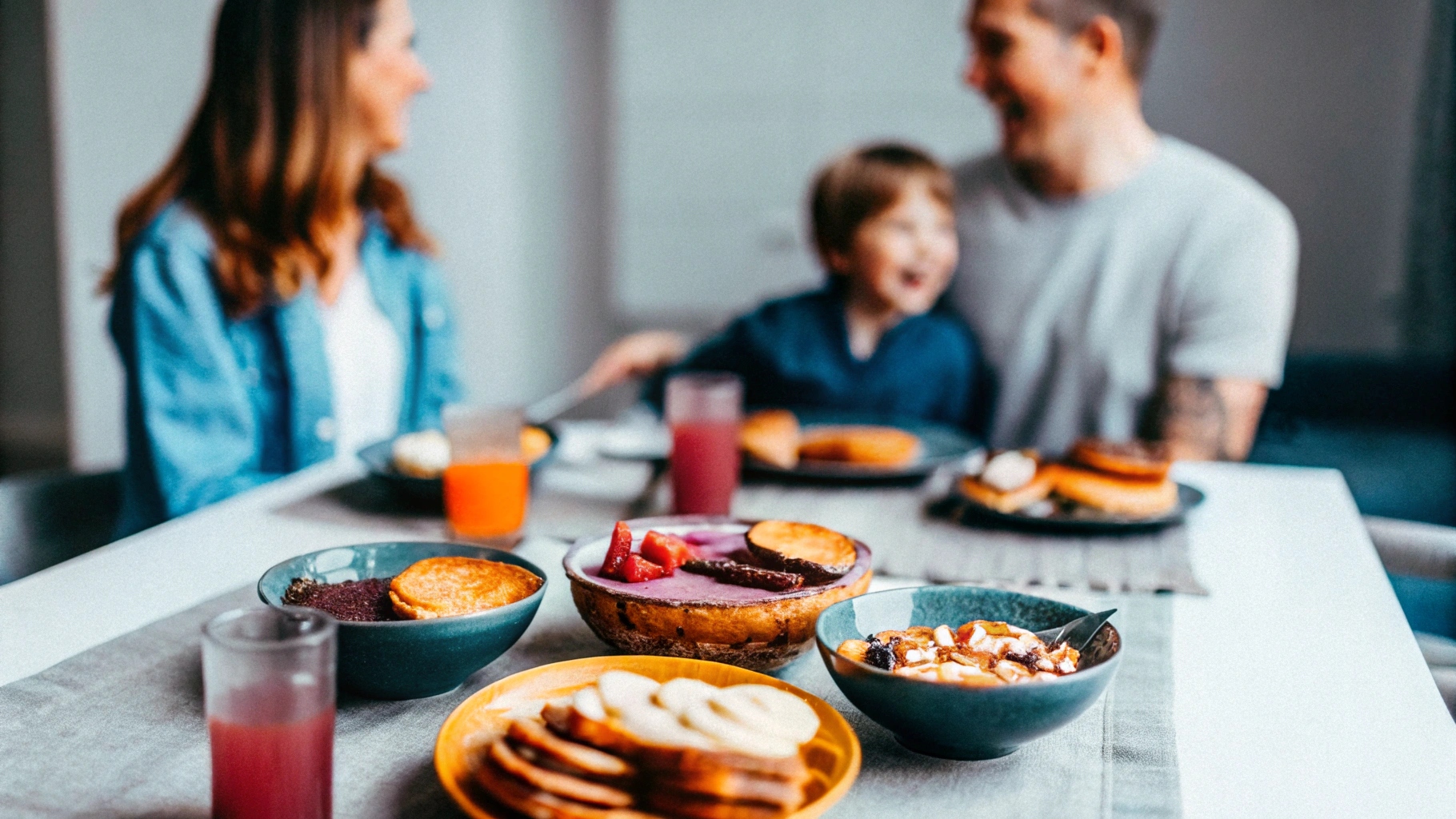 A cozy breakfast table with a variety of sweet dishes, including pancakes, banana bread, and smoothie bowls, surrounded by happy family members