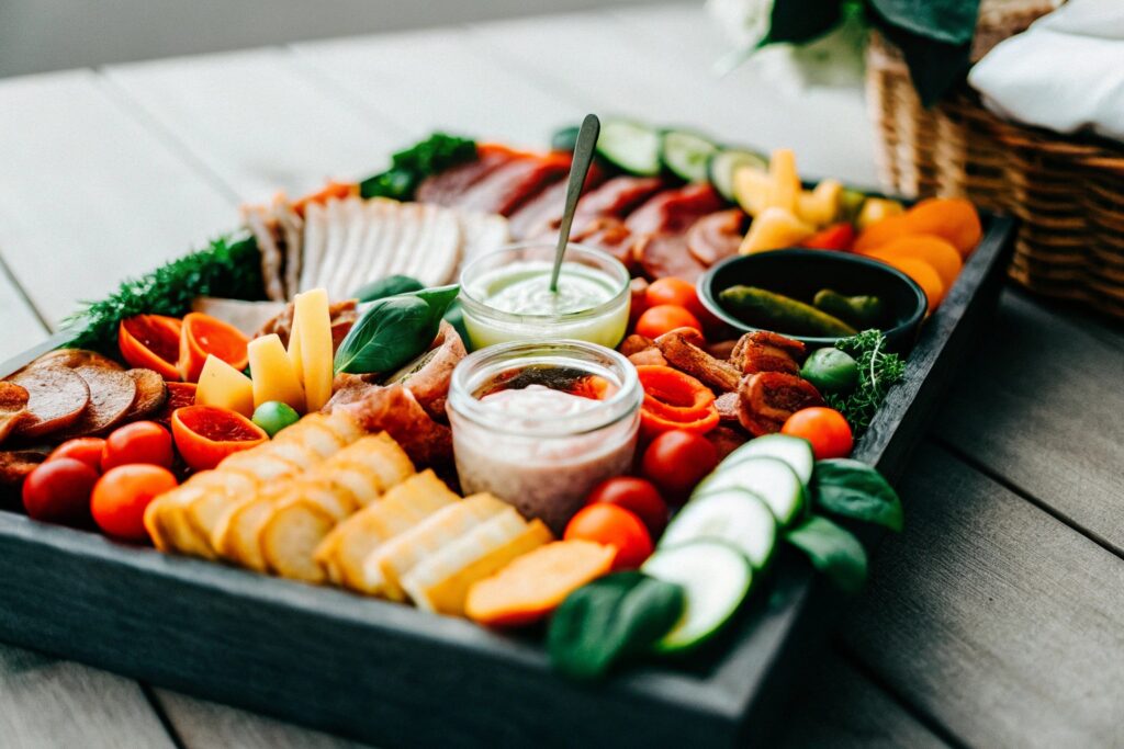 A creative spread of smoked meats, vegetables, and side dishes arranged on a wooden table with various dipping sauces