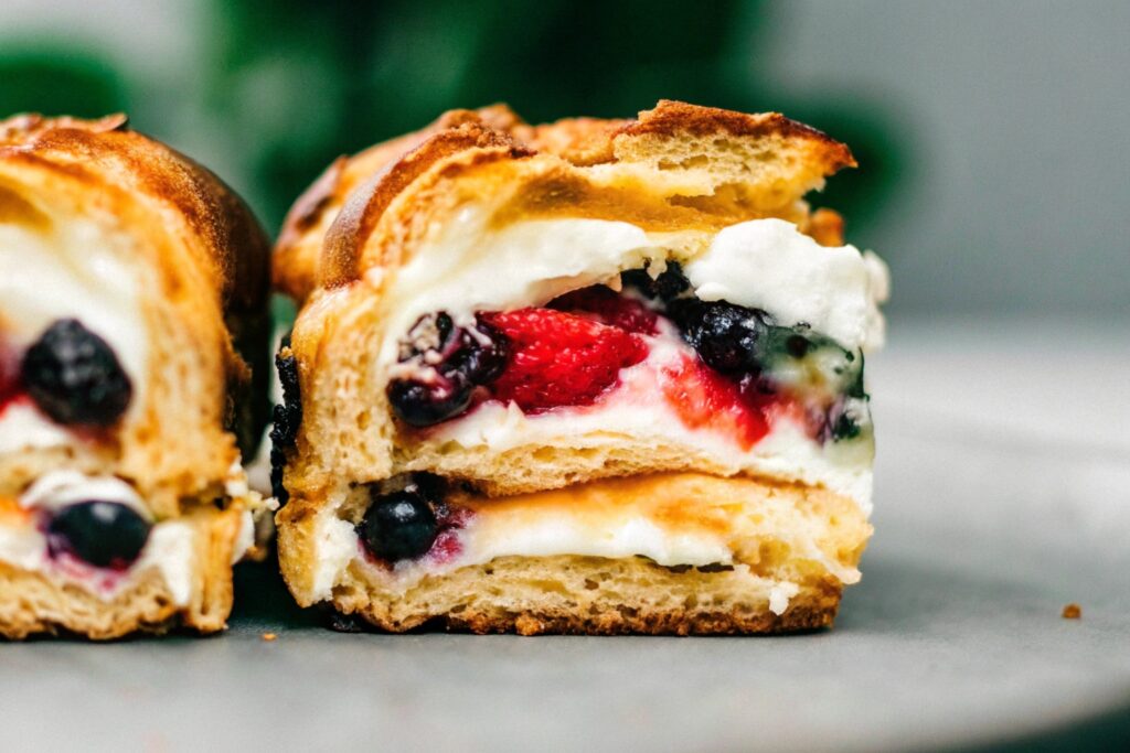 A close-up view of stuffed Hawaiian Roll French Toast, revealing a creamy filling of cream cheese and fresh berries, served on a clean white plate