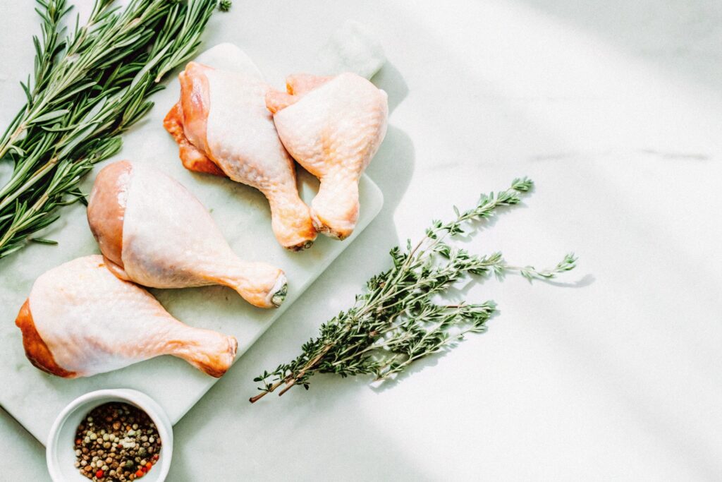 Fresh chicken thighs, bone-in and boneless, arranged on a wooden butcher's board with spices and herbs in small bowls