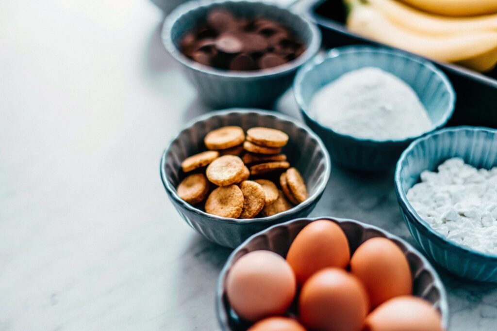 Flat-lay of ingredients for banana pudding ice cream, including bananas, vanilla wafers, heavy cream, and sweetened condensed milk on a marble countertop.