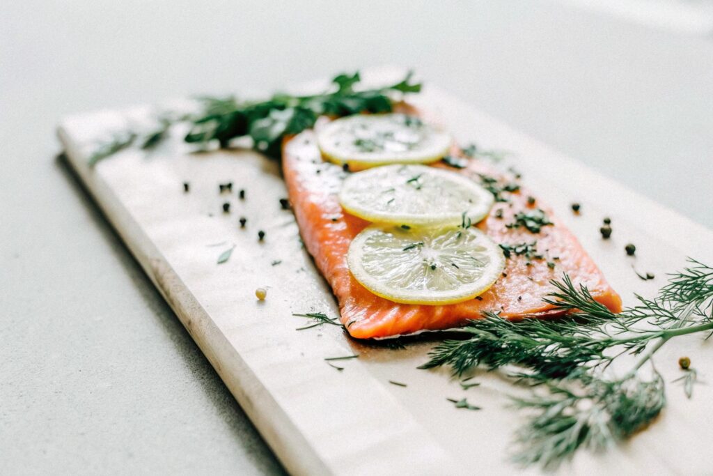 A fresh salmon fillet with lemon slices, herbs, and spices on a wooden cutting board