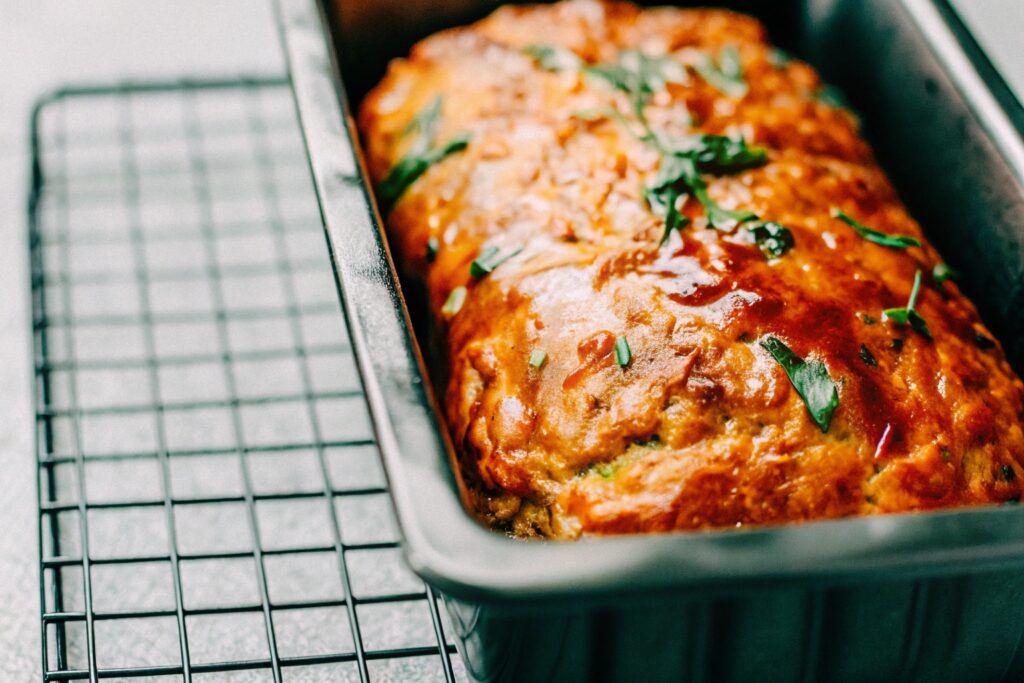 A freshly baked meatloaf in a loaf pan, with a glossy ketchup glaze on top, resting on a cooling rack