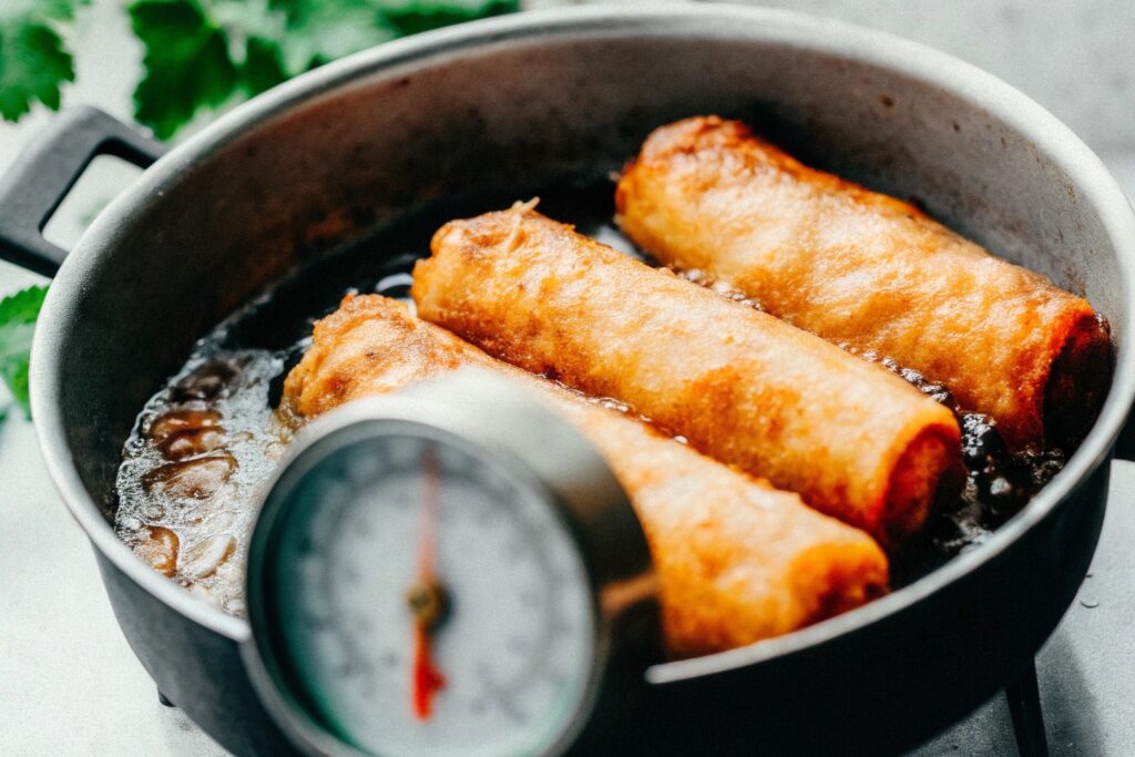 A frying pan with golden egg rolls sizzling in hot oil, with a thermometer showing the perfect frying temperature