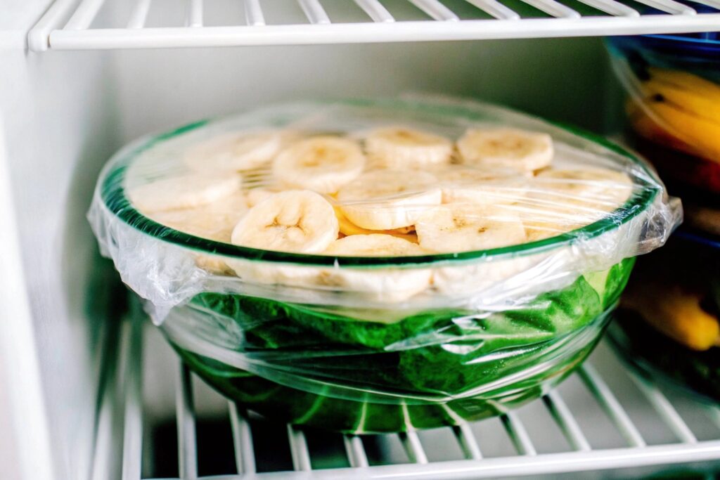 Banana pudding in a glass bowl, covered with plastic wrap, ready to be stored in the freezer.