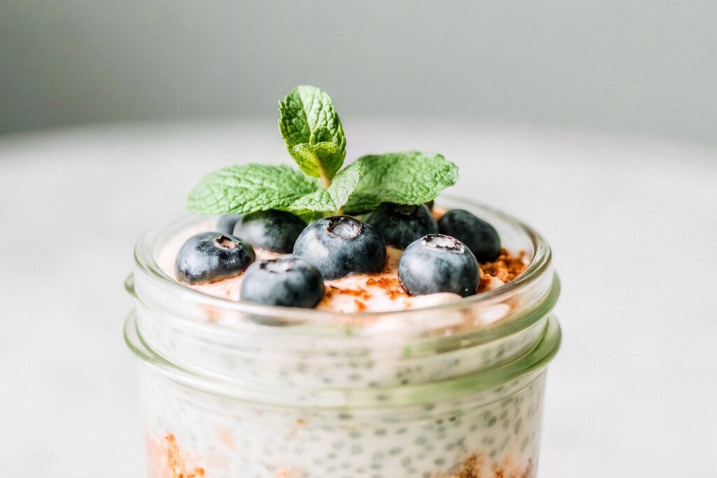 A glass jar filled with creamy chia seed pudding, topped with fresh blueberries, raspberries, and a sprig of mint