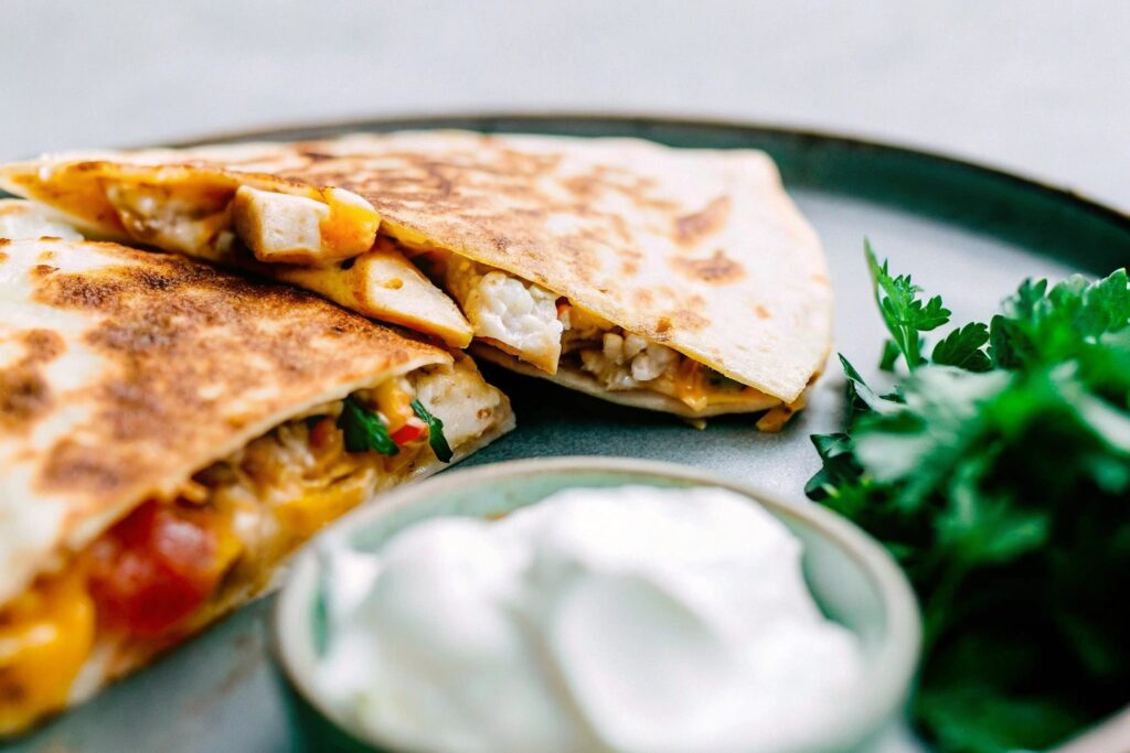 Golden chicken and cheese quesadilla wedges on a rustic plate, served with salsa and sour cream.