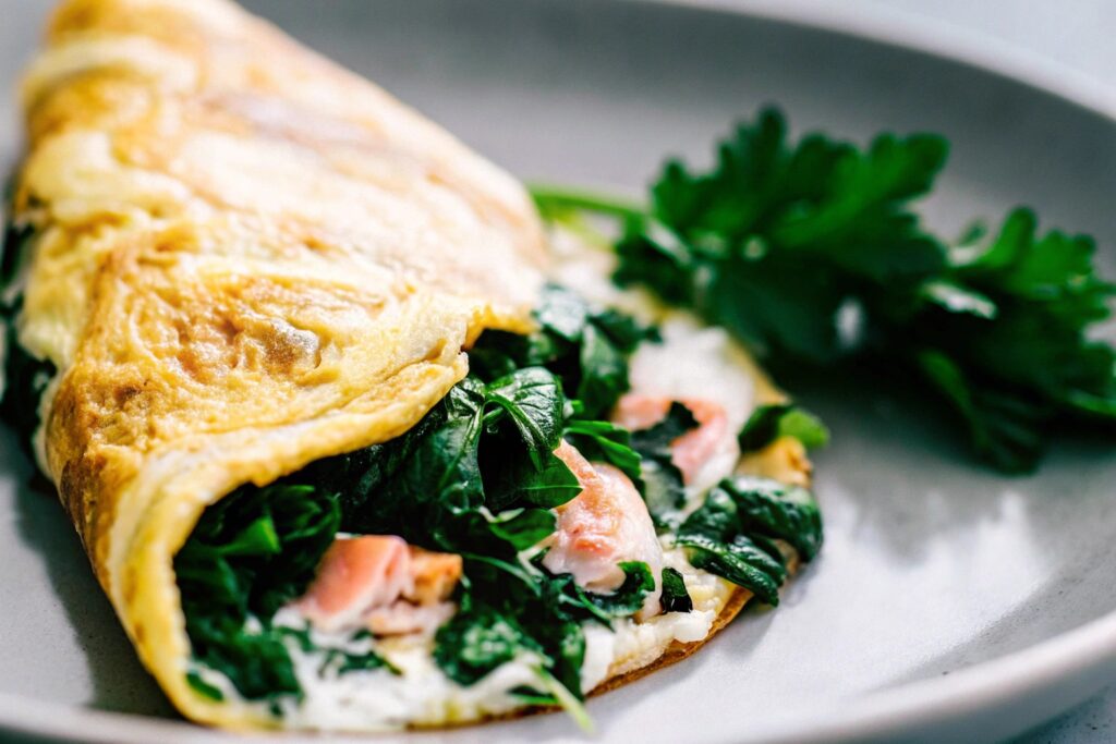 A golden omelet folded over sautéed spinach and flaked salmon, served on a plate with a sprig of fresh parsley for garnish