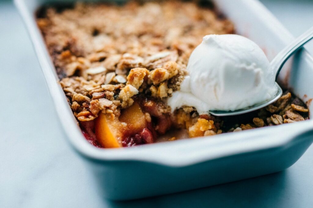 A rustic dish of peach cobbler with golden biscuit topping, served warm with a melting scoop of vanilla ice cream