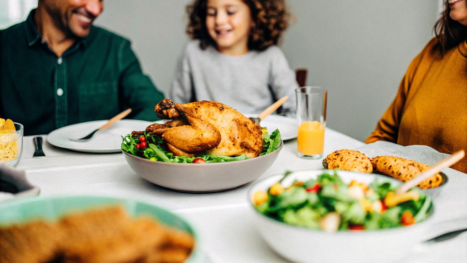 A smiling family gathered around a table, enjoying roasted chicken with a fresh salad and whole-grain bread