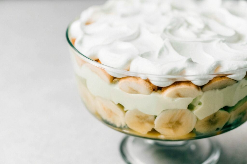 A glass trifle bowl filled with layers of banana slices, vanilla wafers, and creamy custard, topped with fluffy whipped cream