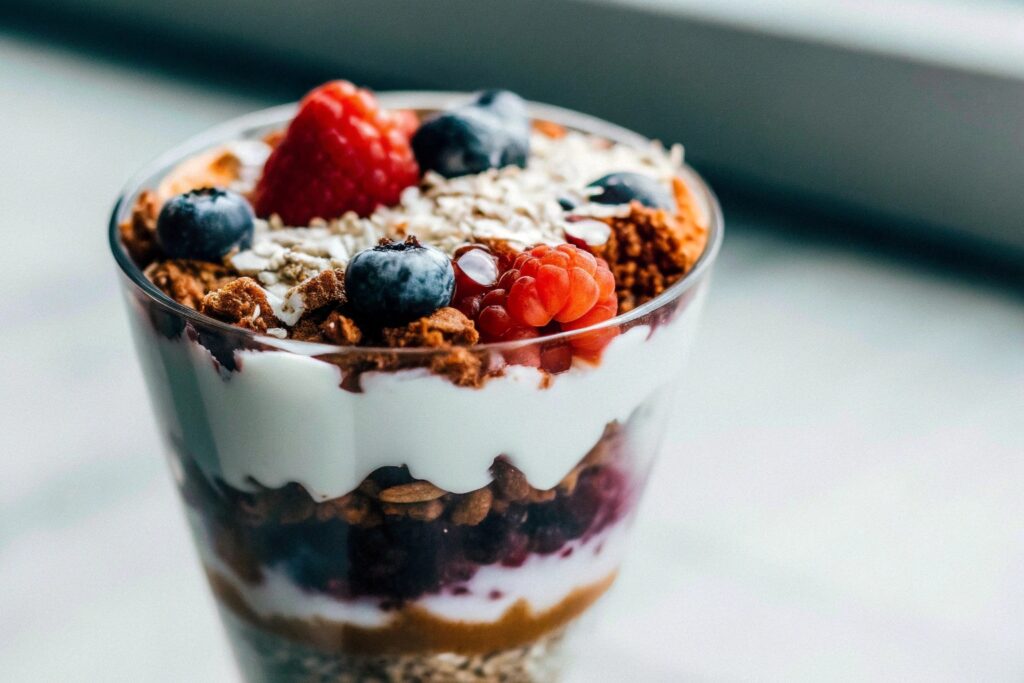 A layered parfait in a clear glass, featuring creamy coconut yogurt, crunchy granola, and fresh mixed berries, garnished with shredded coconut