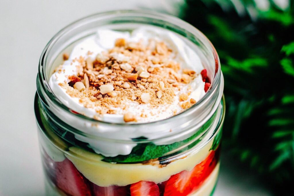 Layered frozen trifle in a clear glass jar with banana pudding, sliced strawberries, and crushed wafer crumbs