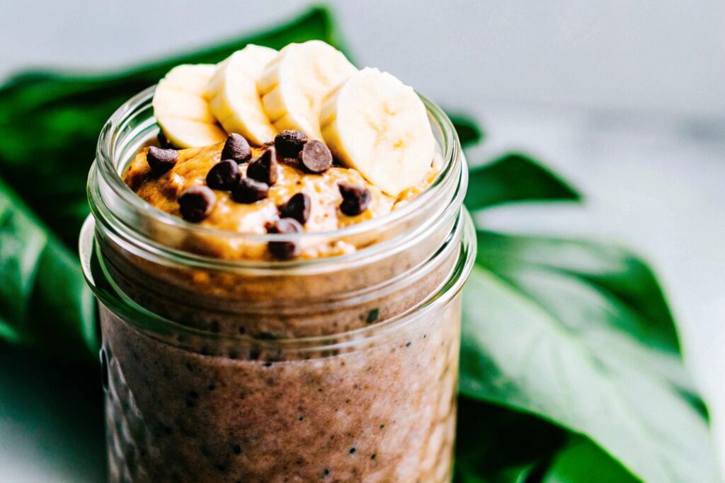 A mason jar filled with chocolate-flavored overnight oats, topped with banana slices and a dollop of peanut butter