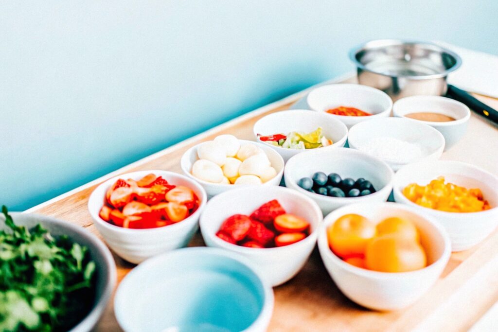 An assortment of ingredients for chicken dressing casserole, including crumbled cornbread, shredded chicken, onions, celery, chicken broth, and canned soups, neatly arranged on a wooden kitchen countertop.