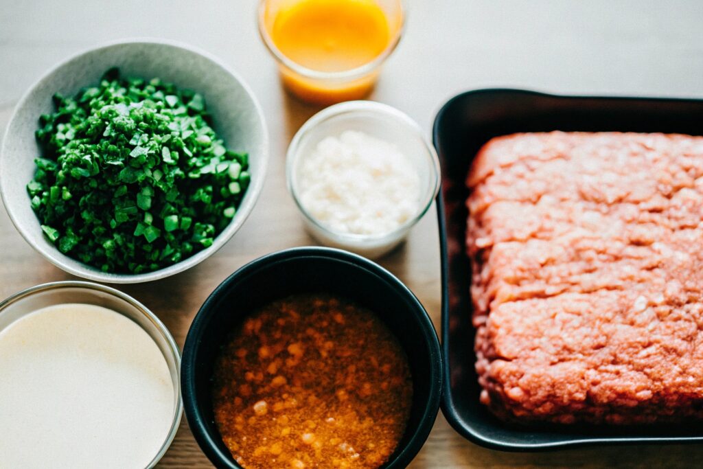 A neatly arranged flat lay of all the meatloaf ingredients on a wooden kitchen counter, including Lipton onion soup mix, ground beef, and measuring cups