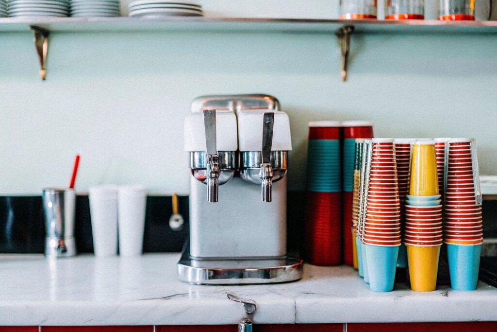 A nostalgic depiction of an old-fashioned soda fountain with a vintage slushy machine surrounded by colorful drink cups