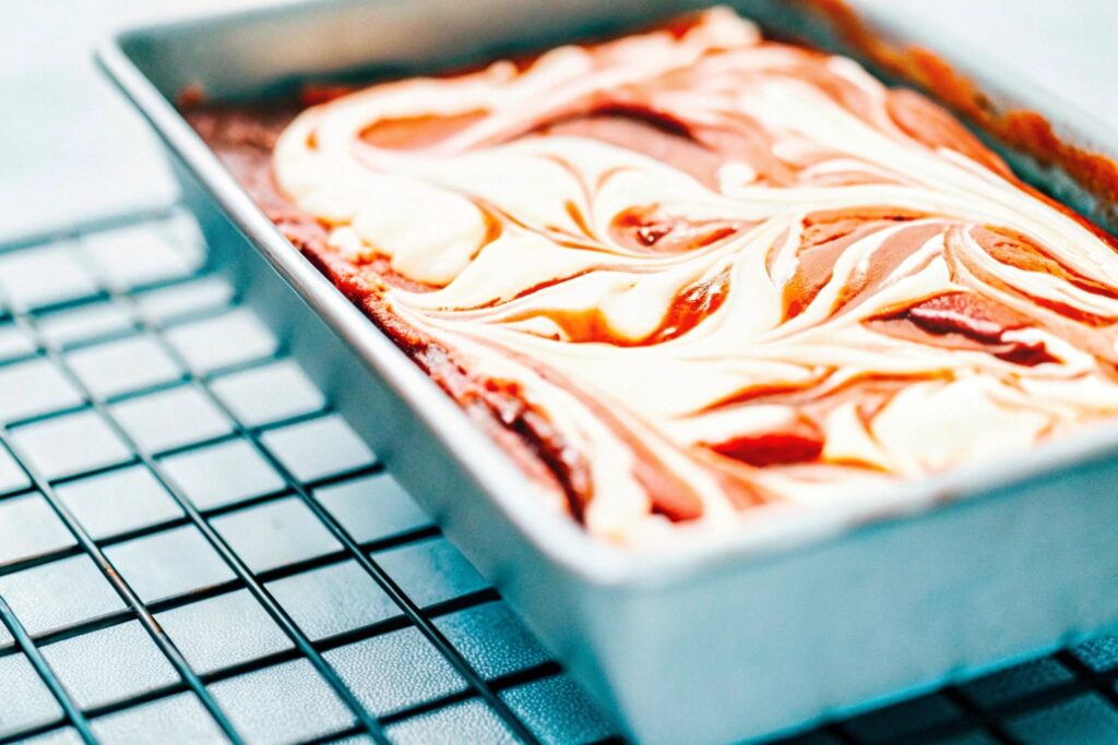 A pan of red velvet brownies fresh from the oven, with a glossy cream cheese swirl on top, ready to be sliced