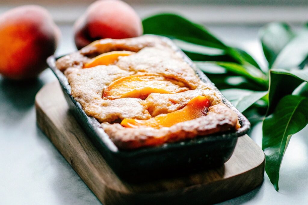 A freshly baked peach cobbler with golden brown cake mix topping and bubbling peach filling in a glass baking dish.
