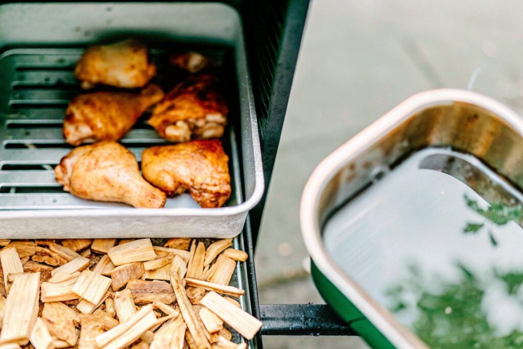 A pellet smoker with chicken thighs placed on the grill, surrounded by a water pan and wood chips ready to smoke