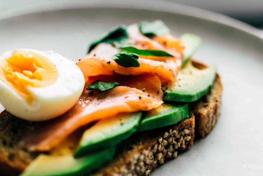 A plate featuring smoked salmon on a slice of multigrain toast with avocado slices and a soft-boiled egg on the side