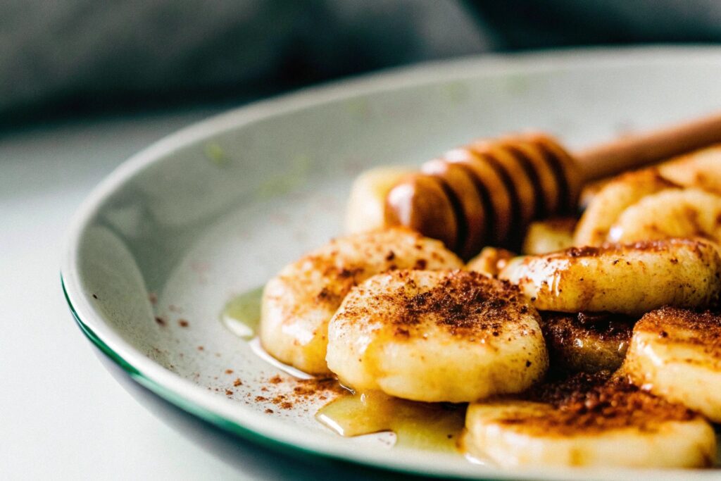 A plate of golden fried bananas garnished with a sprinkle of cinnamon and served with honey on the side