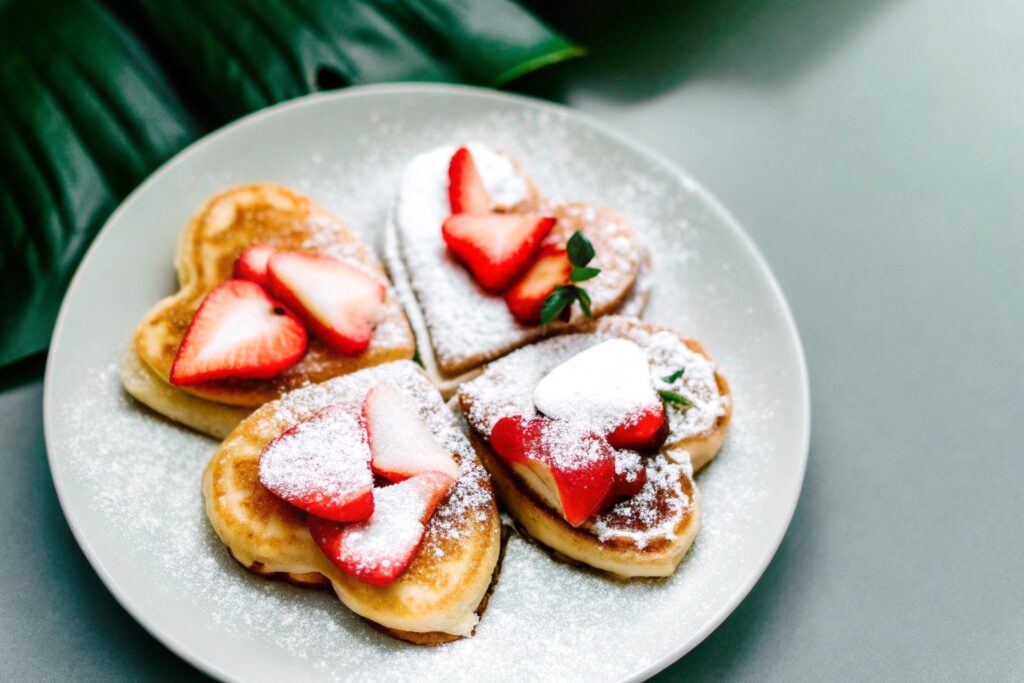 A plate of heart-shaped pancakes topped with fresh strawberries and a dusting of powdered suga