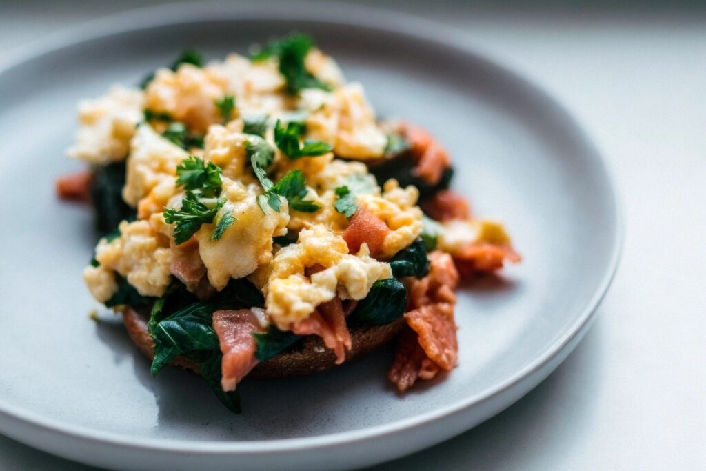 A plate of scrambled eggs mixed with salmon and sautéed spinach, garnished with parsley.