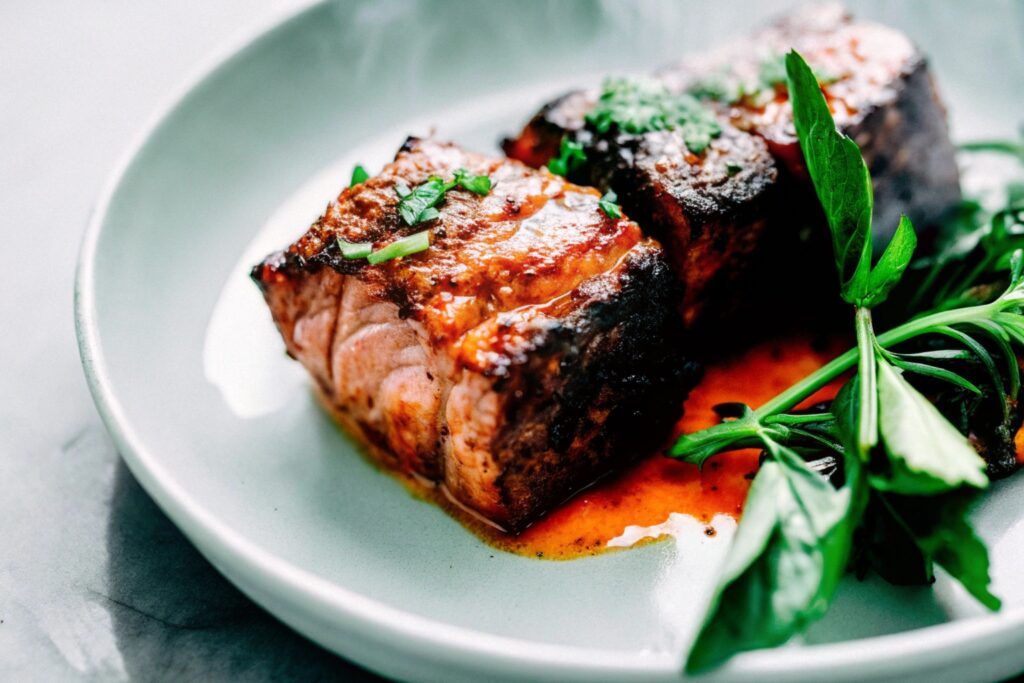 A plated dish featuring boneless beef ribs grilled with a spicy rub and short ribs braised in a rich red wine sauce, served side by side