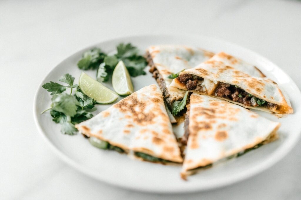 platter of steak quesadillas cut into triangles, served with guacamole, salsa, sour cream, and garnished with lime wedges and cilantro