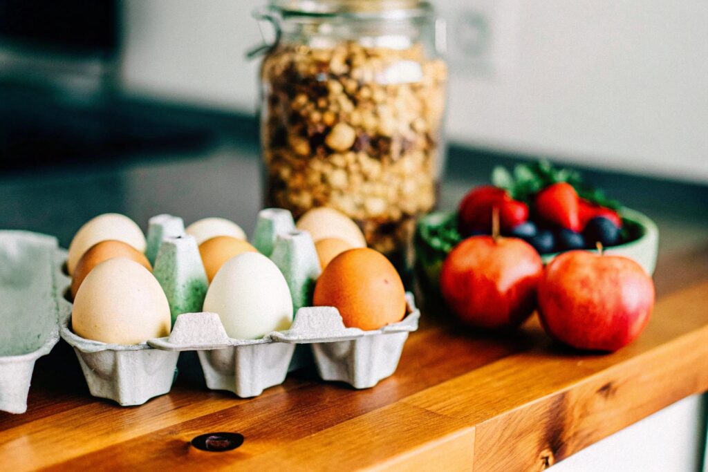 Organic eggs in a carton and a jar of homemade granola with fresh fruit on a rustic kitchen counter