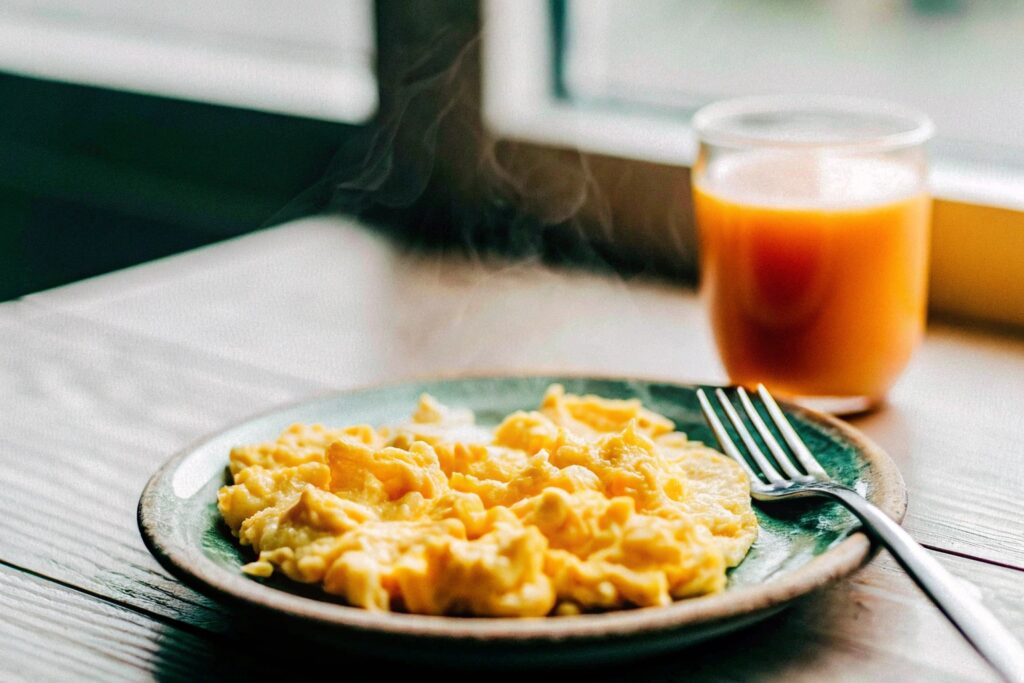  A rustic kitchen counter featuring a plate of freshly scrambled eggs garnished with parsley, accompanied by a fork and a glass of orange juice