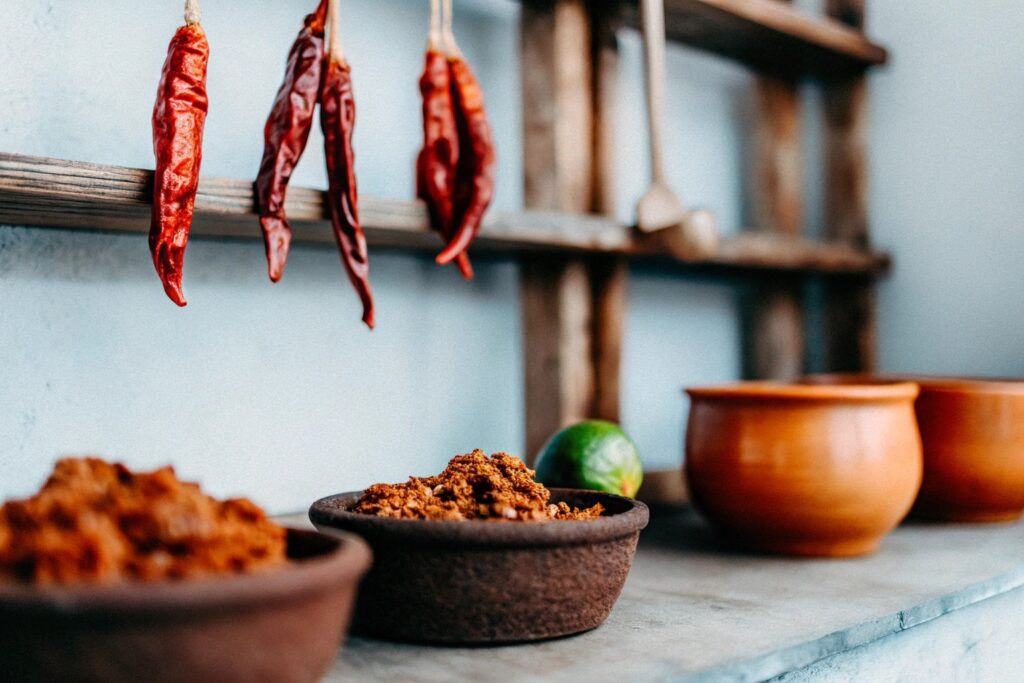 A rustic setup featuring a bowl of cooked ground beef surrounded by dried chipotle peppers, traditional Mexican spices, and fresh lime wedges