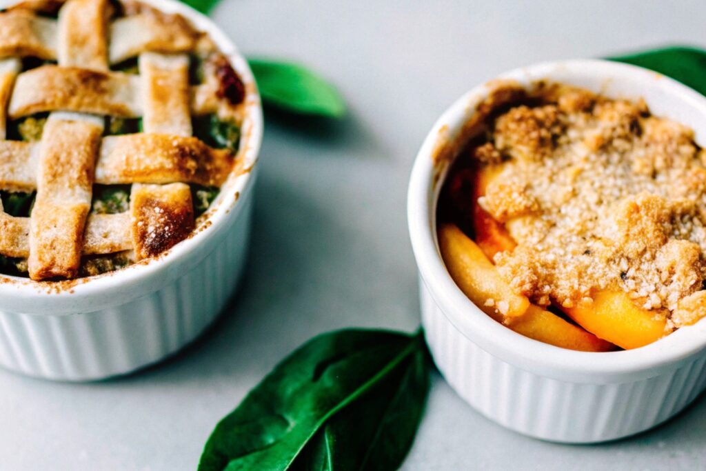 A peach crumble in a white baking dish with a crunchy oat and nut topping, garnished with a dollop of whipped cream.