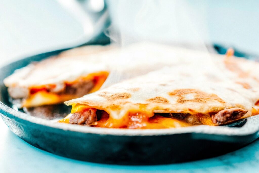 A sizzling quesadilla in a cast-iron skillet, with melted cheese and slices of steak visible, paired with a golden tortilla