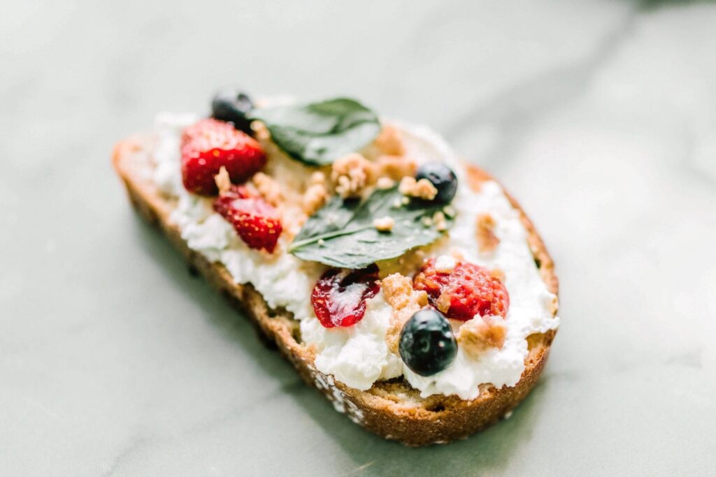 A slice of toasted whole-grain bread spread with cream cheese, topped with fresh berries and a sprinkle of crushed graham crackers