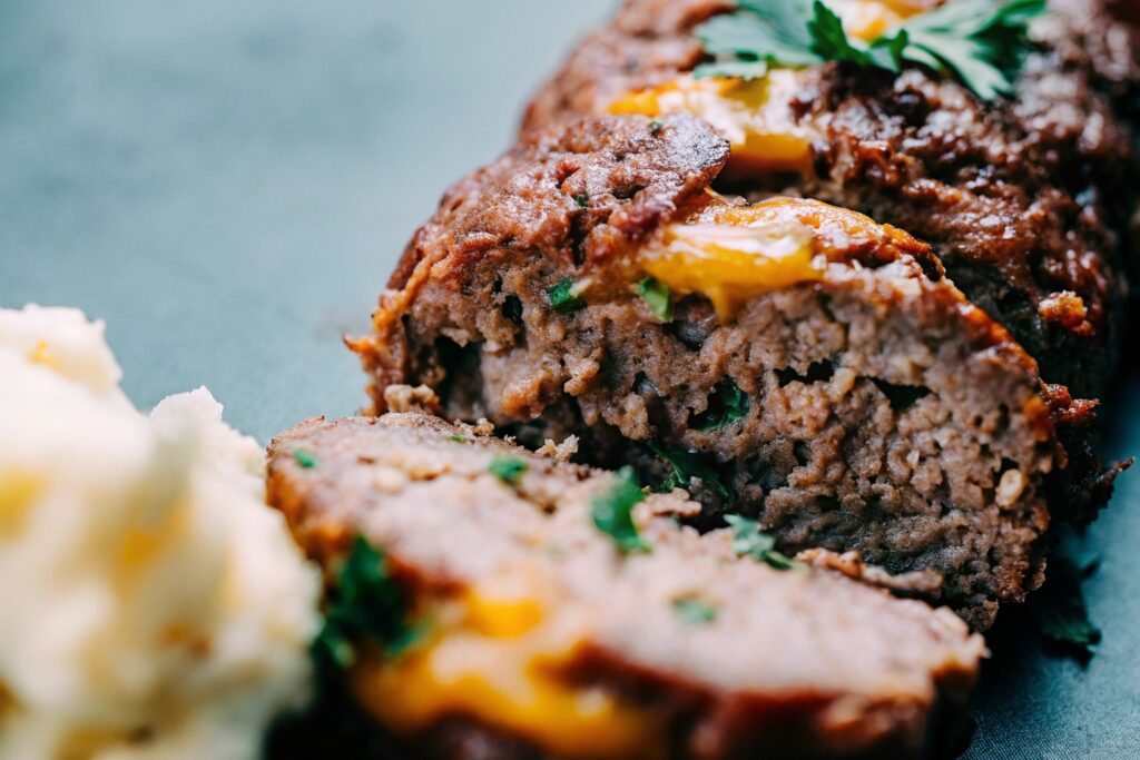 A sliced meatloaf filled with gooey melted cheese and garnished with fresh parsley, served with a side of mashed potatoes