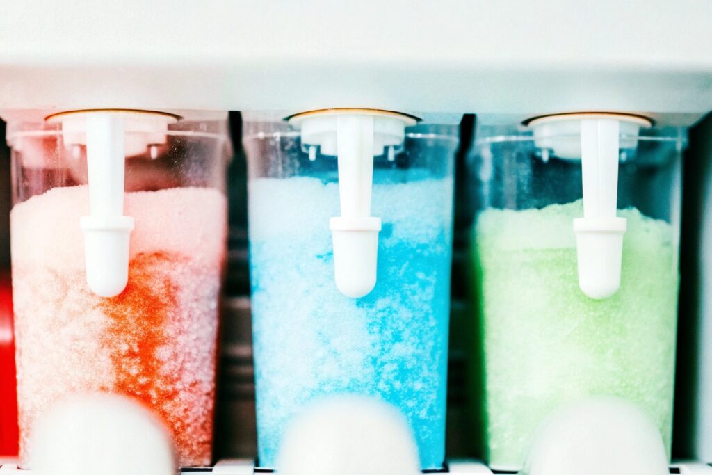 A slushy machine with colorful drinks being stirred, showing the icy texture forming inside