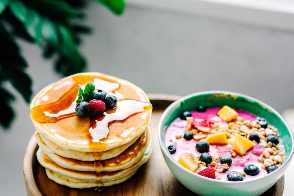 A stack of golden pancakes topped with syrup and berries, next to a smoothie bowl with vibrant toppings