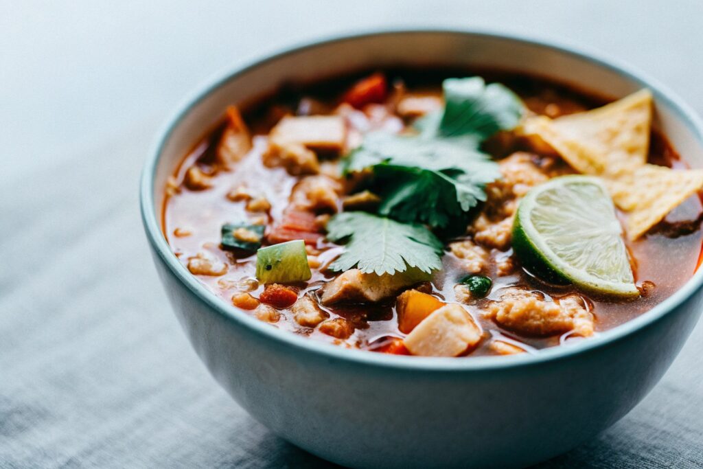 A steaming bowl of chicken taco soup served with lime wedges, tortilla chips, and fresh cilantro, reflecting its Mexican roots.