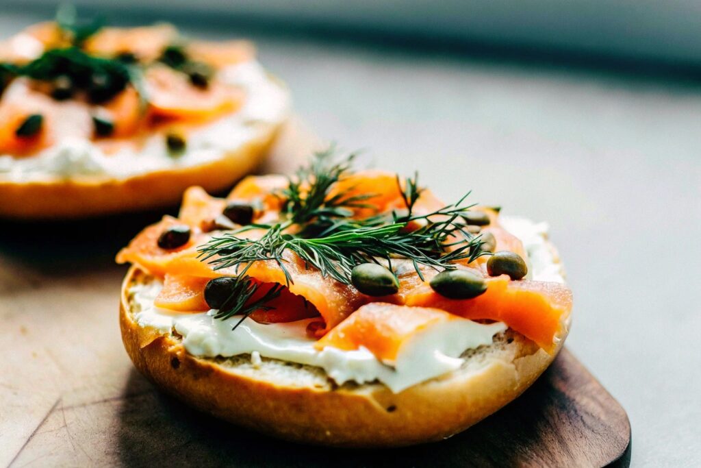 A toasted bagel topped with cream cheese, smoked salmon, capers, and fresh dill, served on a wooden board