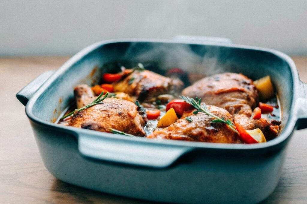 A traditional French-style chicken casserole with vegetables and herbs, simmering in an uncovered ceramic dish