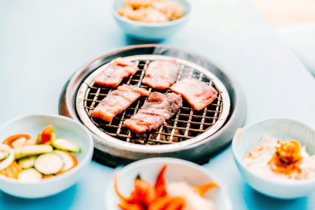 A traditional Korean barbecue setup featuring marinated short ribs sizzling on a grill alongside small side dishes (banchan)