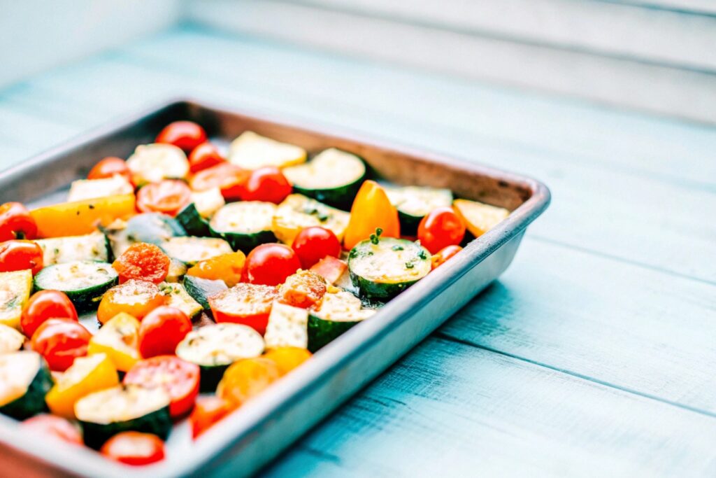 of roasted zucchini, cherry tomatoes, and bell peppers sprinkled with fresh herbs, placed on a rustic wooden table