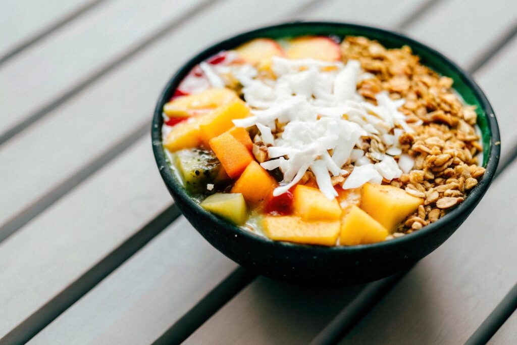 A vibrant tropical smoothie bowl topped with granola, shredded coconut, sliced kiwi, and fresh pineapple chunks, served on a wooden table