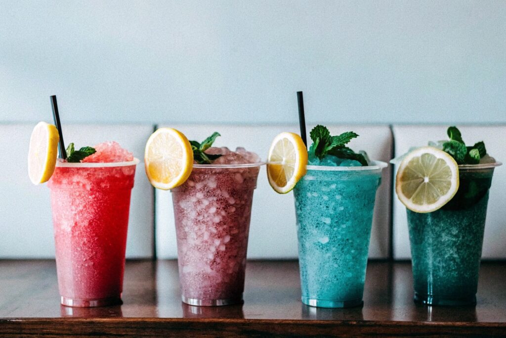 A variety of slushies on display, featuring bright fruit flavors and garnishes like lemon slices and mint leaves.